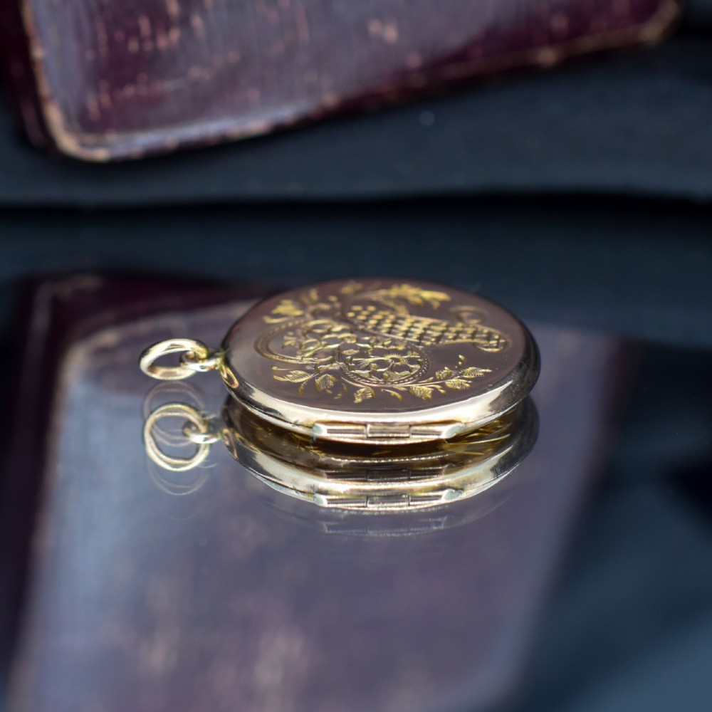 A circular antique yellow gold locket featuring intricate hand engraving of a flower basket motif. View VIII
