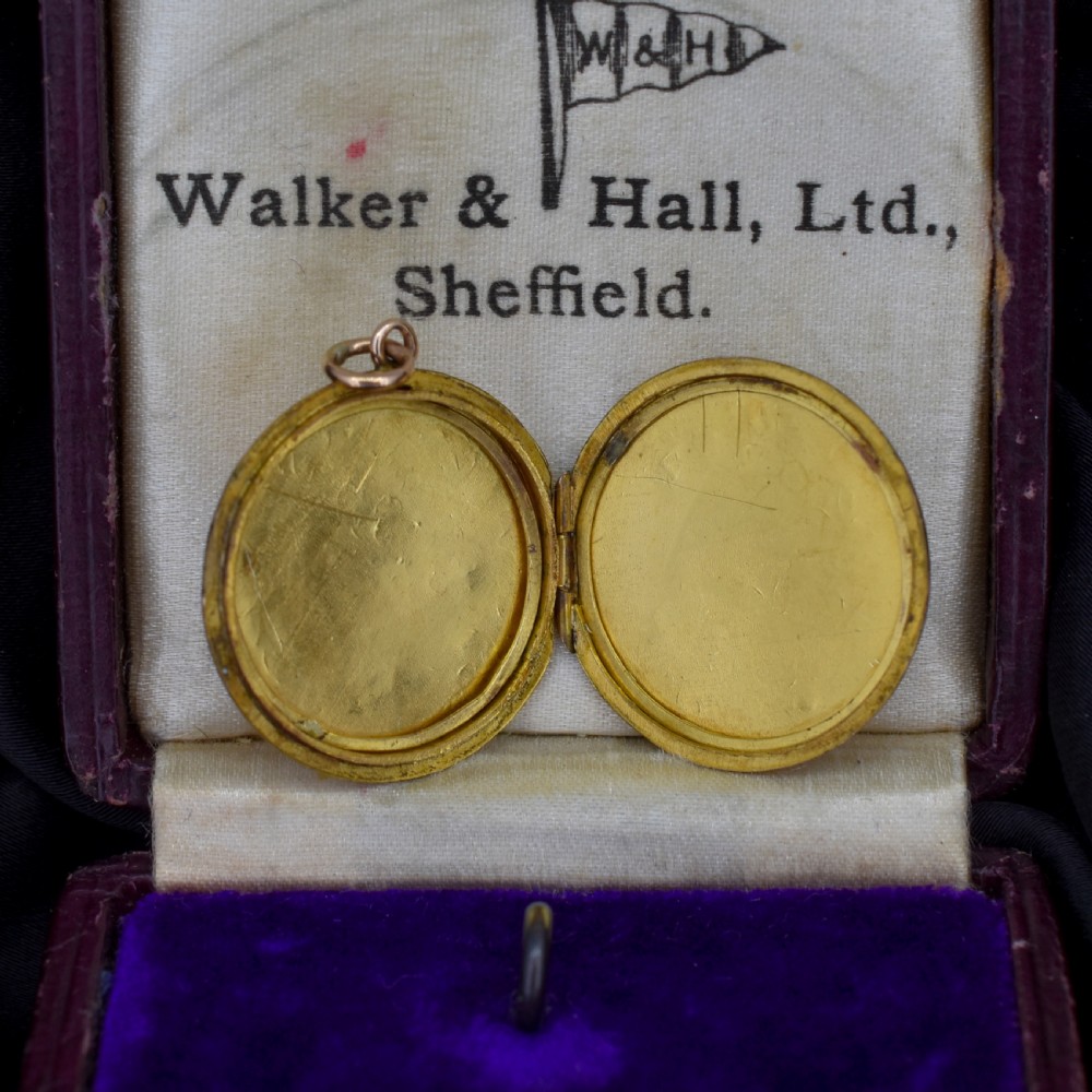 A circular antique yellow gold locket featuring intricate hand engraving of a flower basket motif. View X