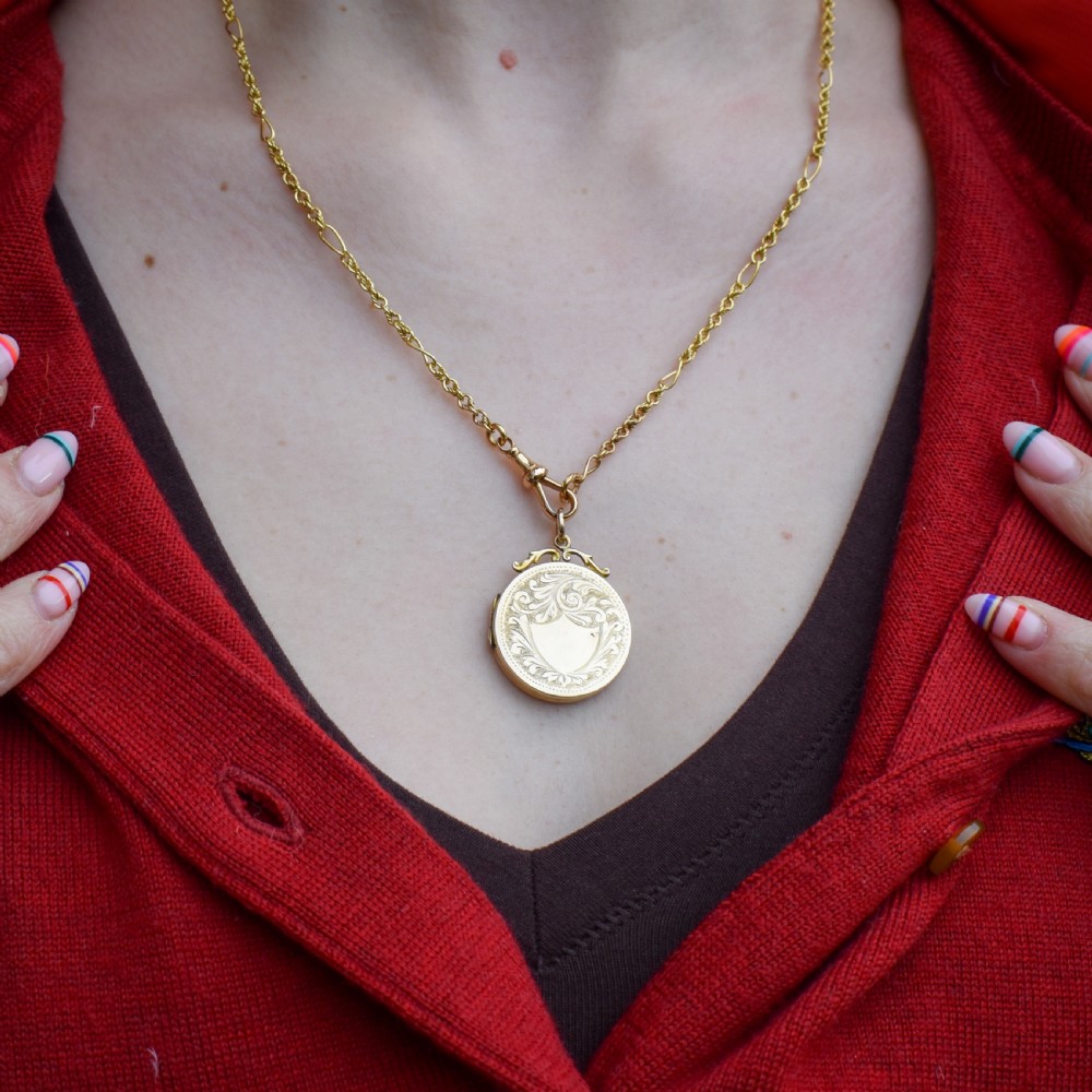 A circular 9ct yellow gold antique locket featuring hand-engraved foliate scrollwork and a central blank shield cartouche with a ornate top loop. View II