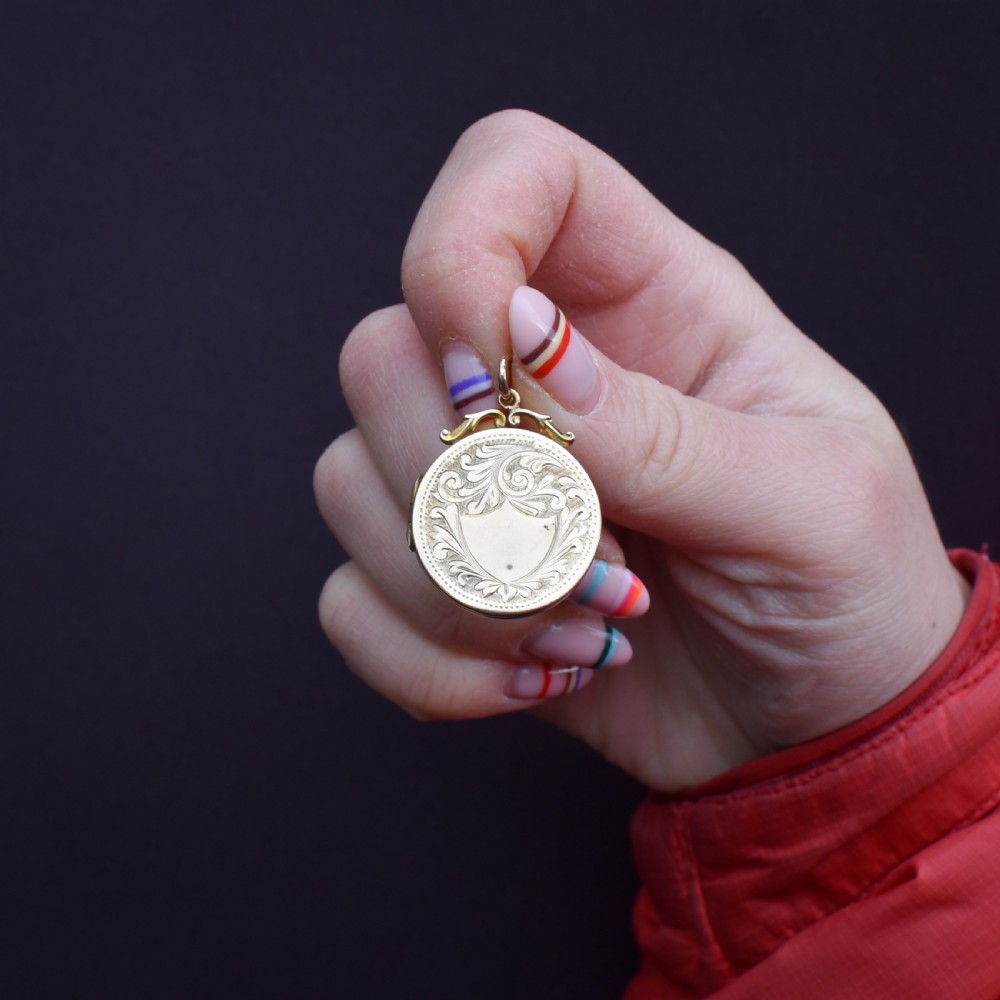 A circular 9ct yellow gold antique locket featuring hand-engraved foliate scrollwork and a central blank shield cartouche with a ornate top loop. View III
