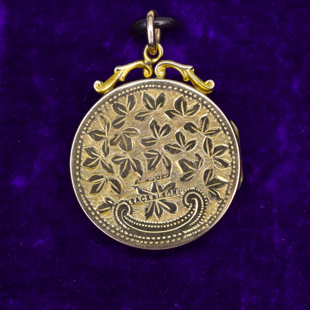 A circular 9ct yellow gold antique locket featuring hand-engraved foliate scrollwork and a central blank shield cartouche with a ornate top loop. View V