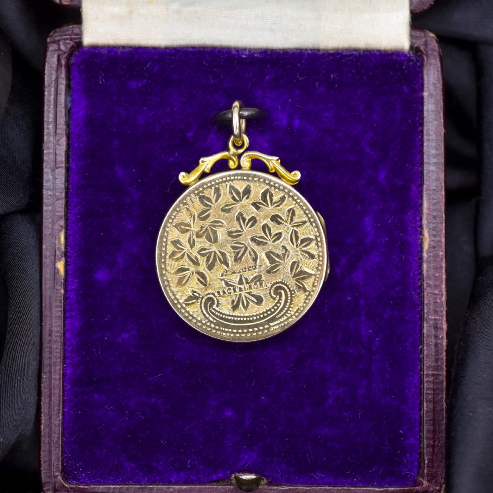 A circular 9ct yellow gold antique locket featuring hand-engraved foliate scrollwork and a central blank shield cartouche with a ornate top loop. View VI