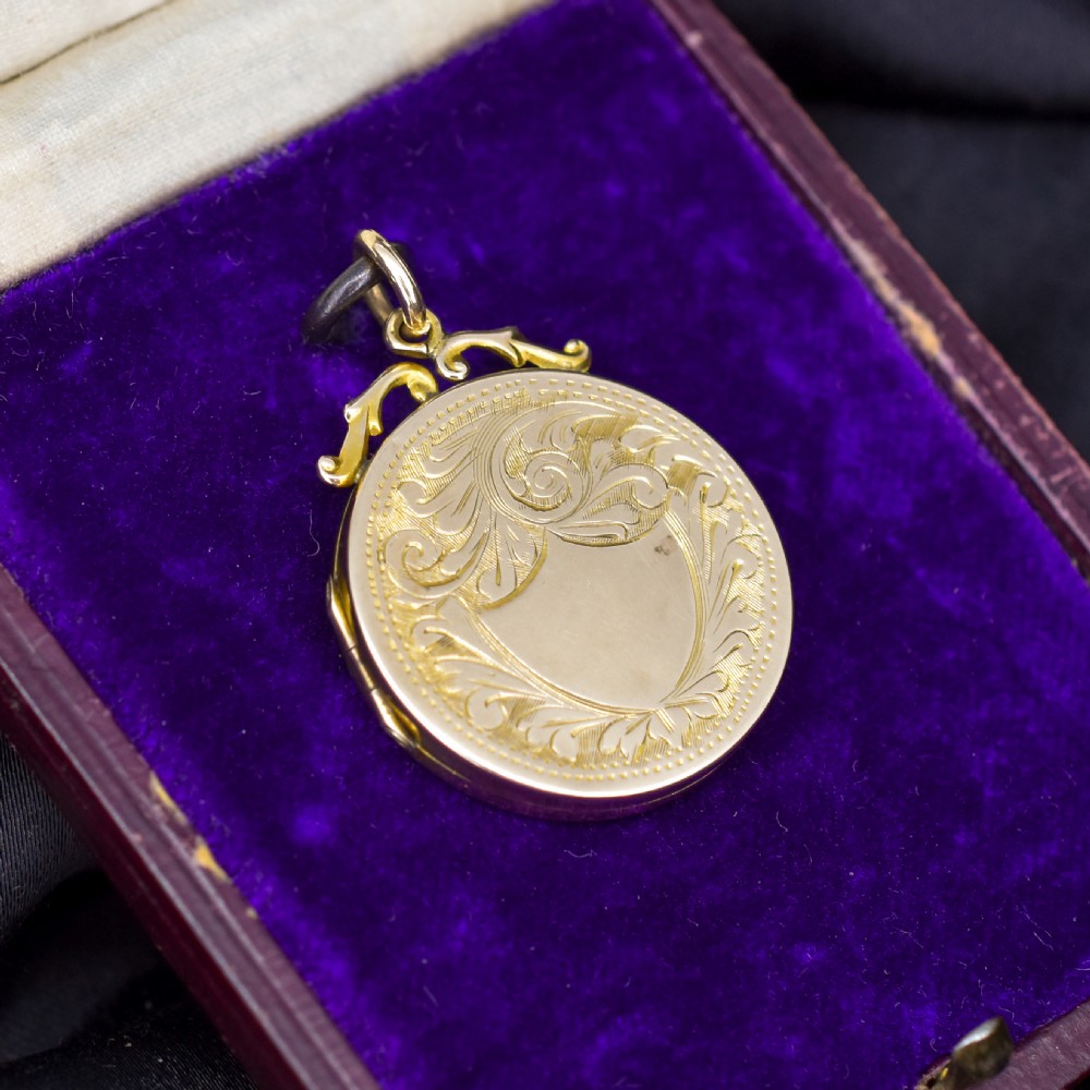 A circular 9ct yellow gold antique locket featuring hand-engraved foliate scrollwork and a central blank shield cartouche with a ornate top loop. View VII