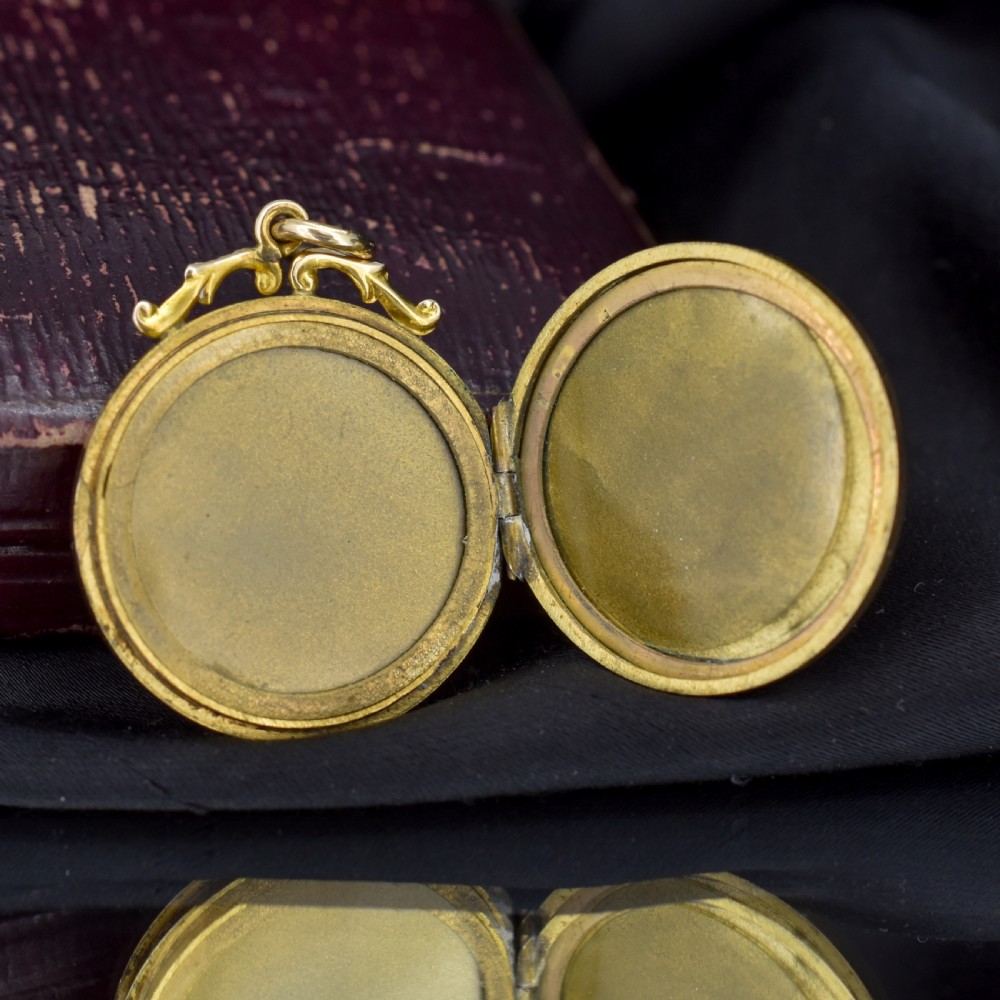 A circular 9ct yellow gold antique locket featuring hand-engraved foliate scrollwork and a central blank shield cartouche with a ornate top loop. View X