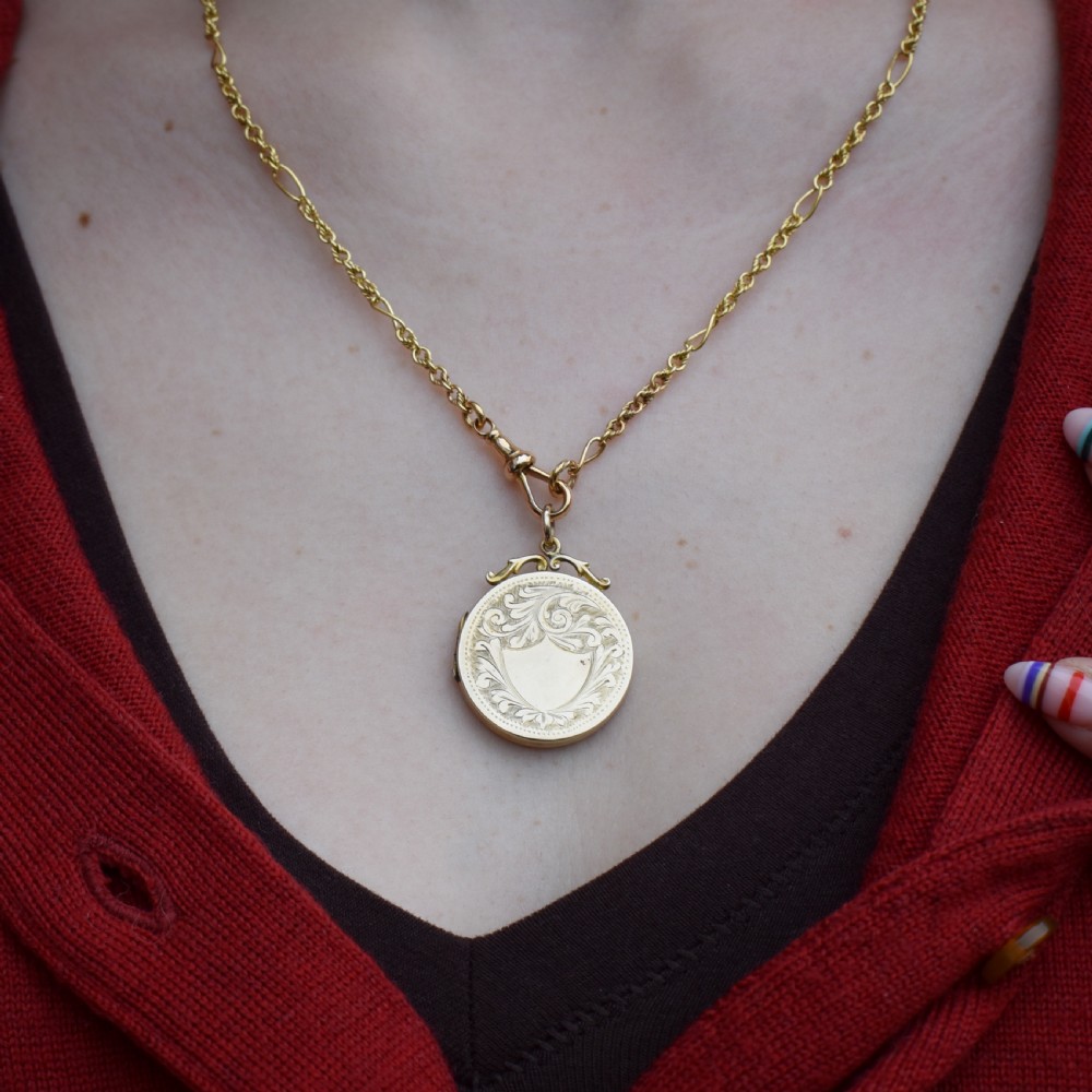 A circular 9ct yellow gold antique locket featuring hand-engraved foliate scrollwork and a central blank shield cartouche with a ornate top loop. View XI