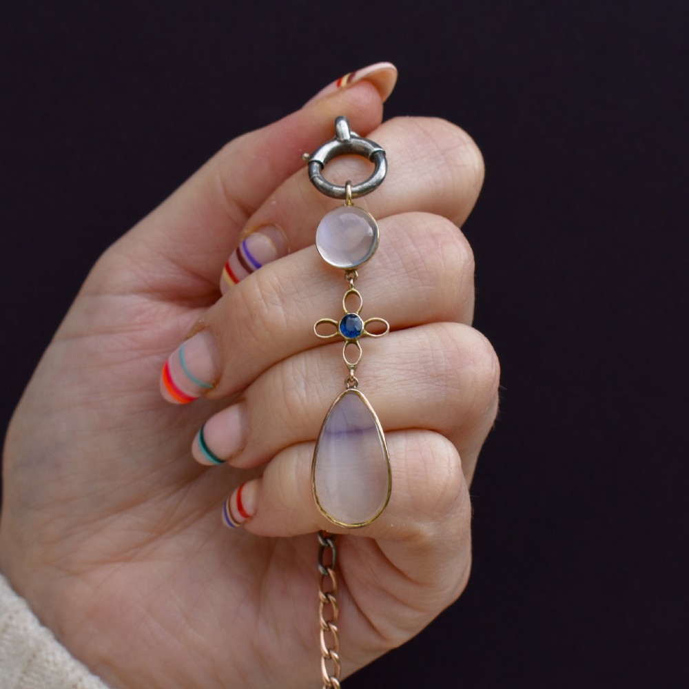 An antique 9ct gold drop pendant featuring a round moonstone cabochon, a centre quatrefoil motif with a blue sapphire, and a teardrop moonstone drop. View II