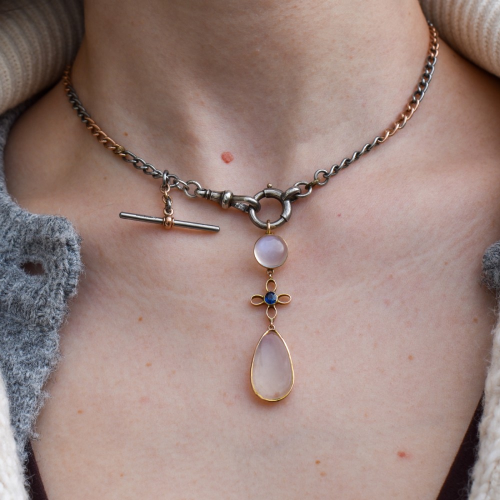 An antique 9ct gold drop pendant featuring a round moonstone cabochon, a centre quatrefoil motif with a blue sapphire, and a teardrop moonstone drop. View V