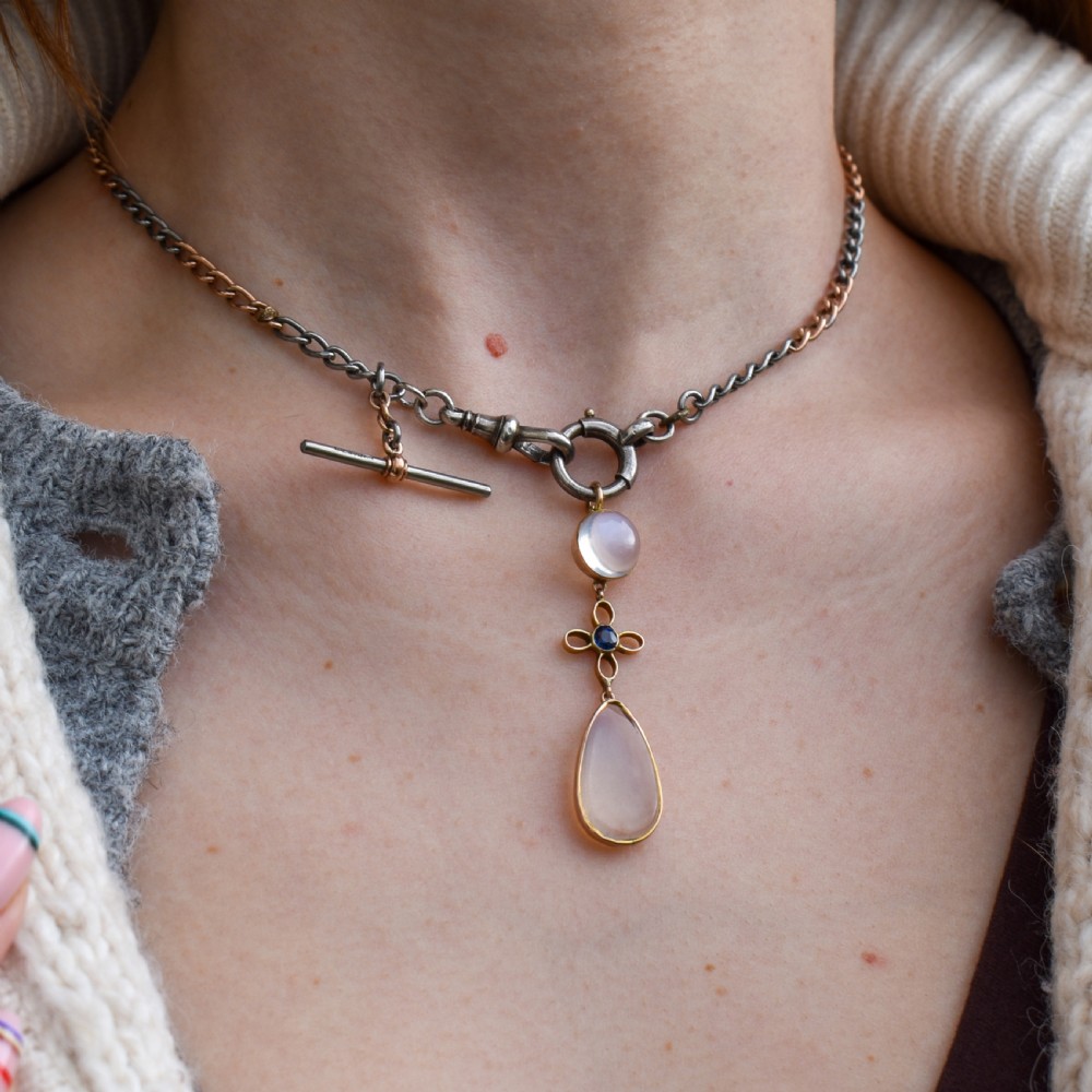 An antique 9ct gold drop pendant featuring a round moonstone cabochon, a centre quatrefoil motif with a blue sapphire, and a teardrop moonstone drop. View VI