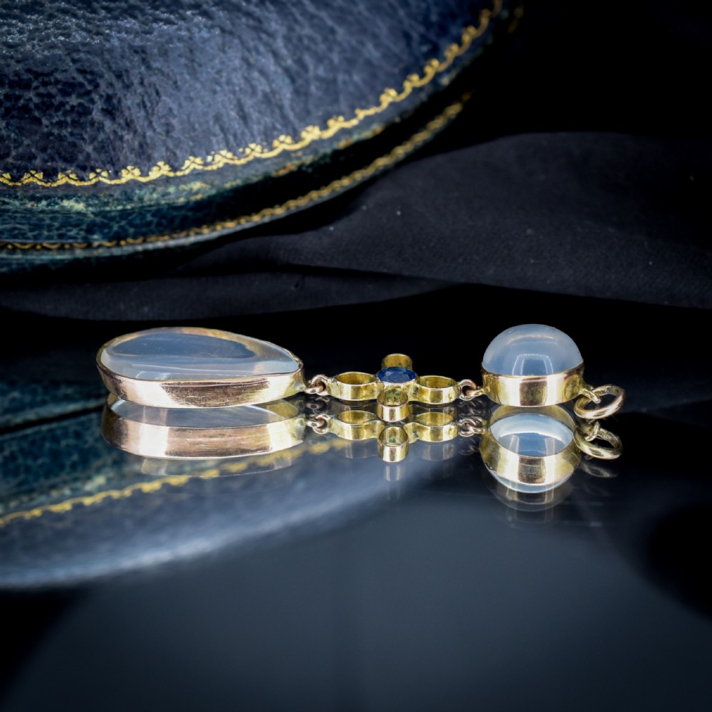 An antique 9ct gold drop pendant featuring a round moonstone cabochon, a centre quatrefoil motif with a blue sapphire, and a teardrop moonstone drop. View X