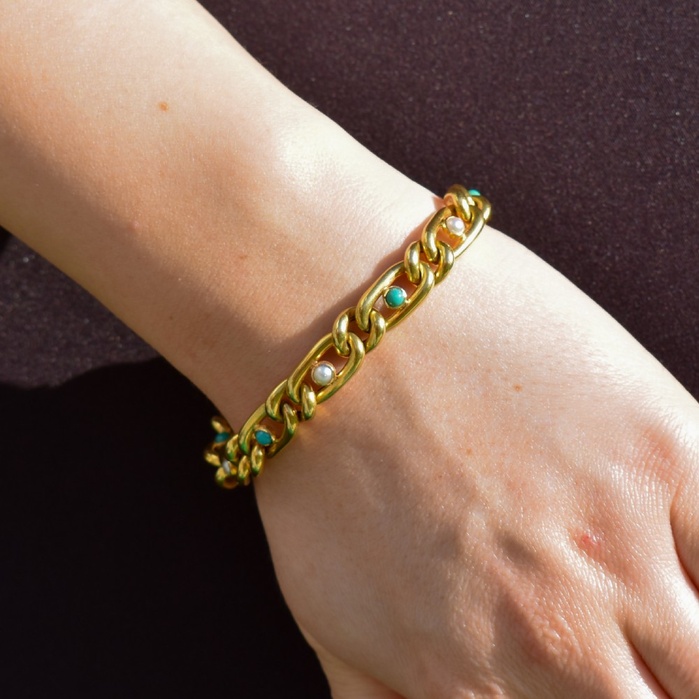 An antique 15ct yellow gold curb link bracelet featuring inset seed pearls and round turquoise cabochons with an attached safety chain. View III