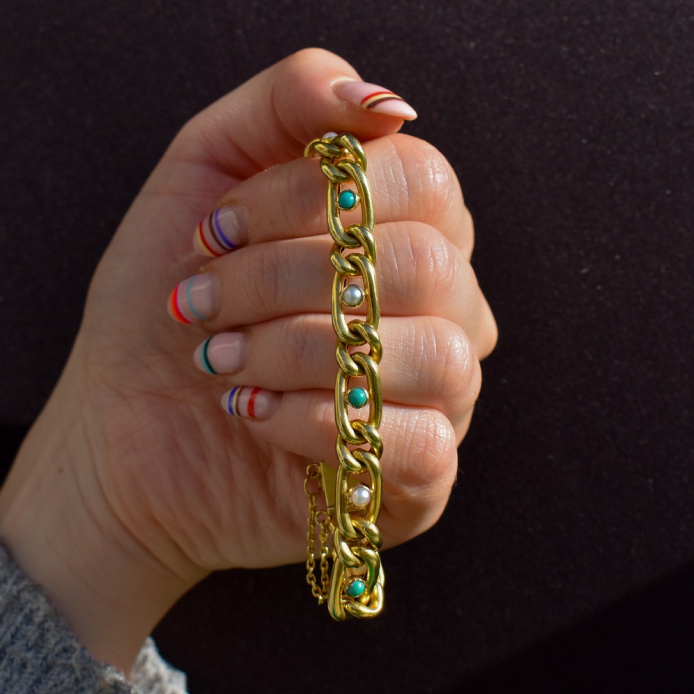 An antique 15ct yellow gold curb link bracelet featuring inset seed pearls and round turquoise cabochons with an attached safety chain. View V