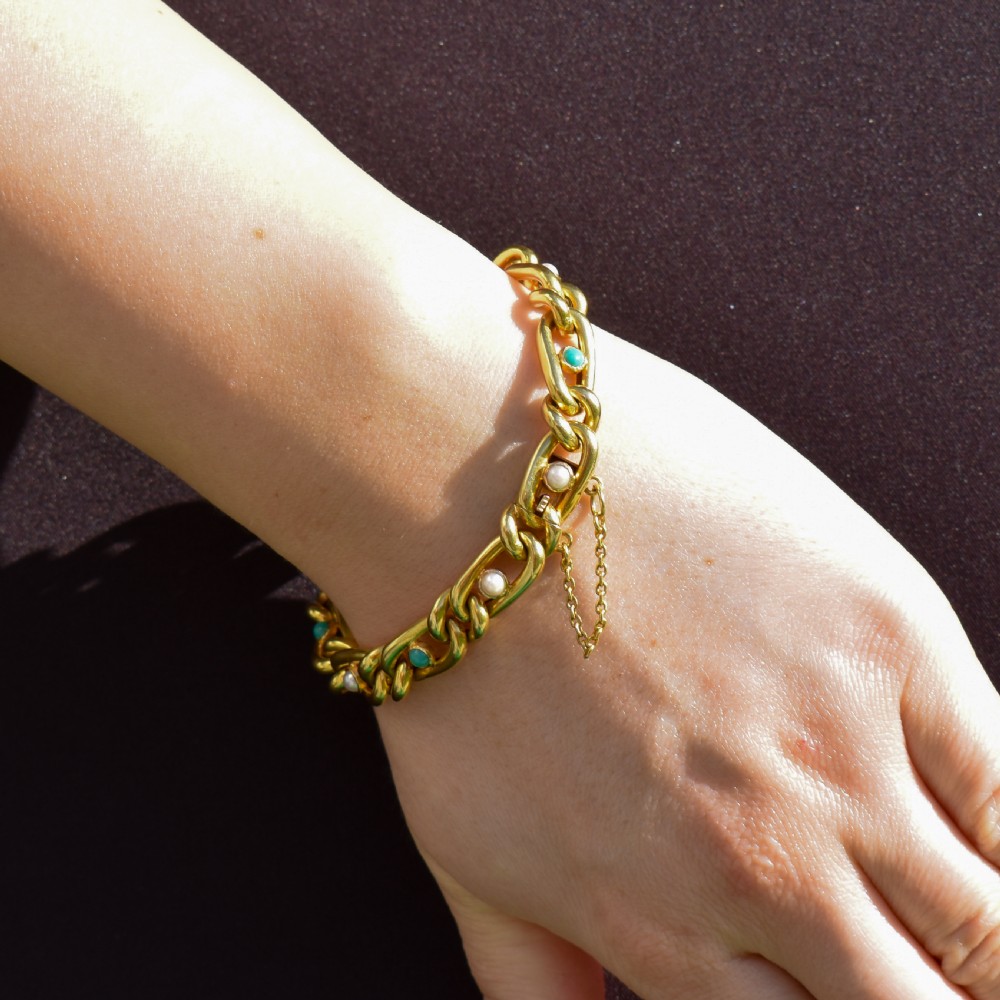 An antique 15ct yellow gold curb link bracelet featuring inset seed pearls and round turquoise cabochons with an attached safety chain. View VI