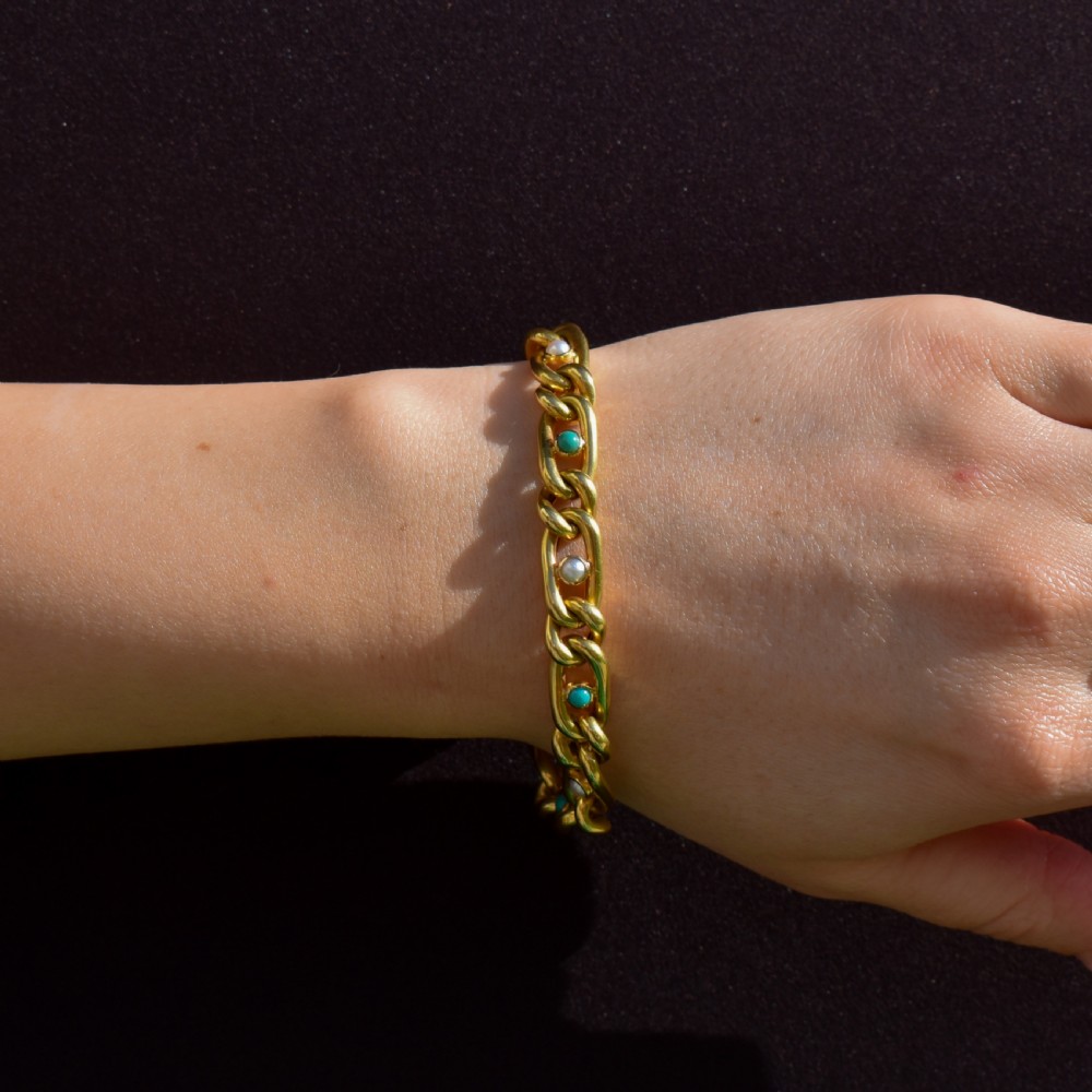 An antique 15ct yellow gold curb link bracelet featuring inset seed pearls and round turquoise cabochons with an attached safety chain. View VIII
