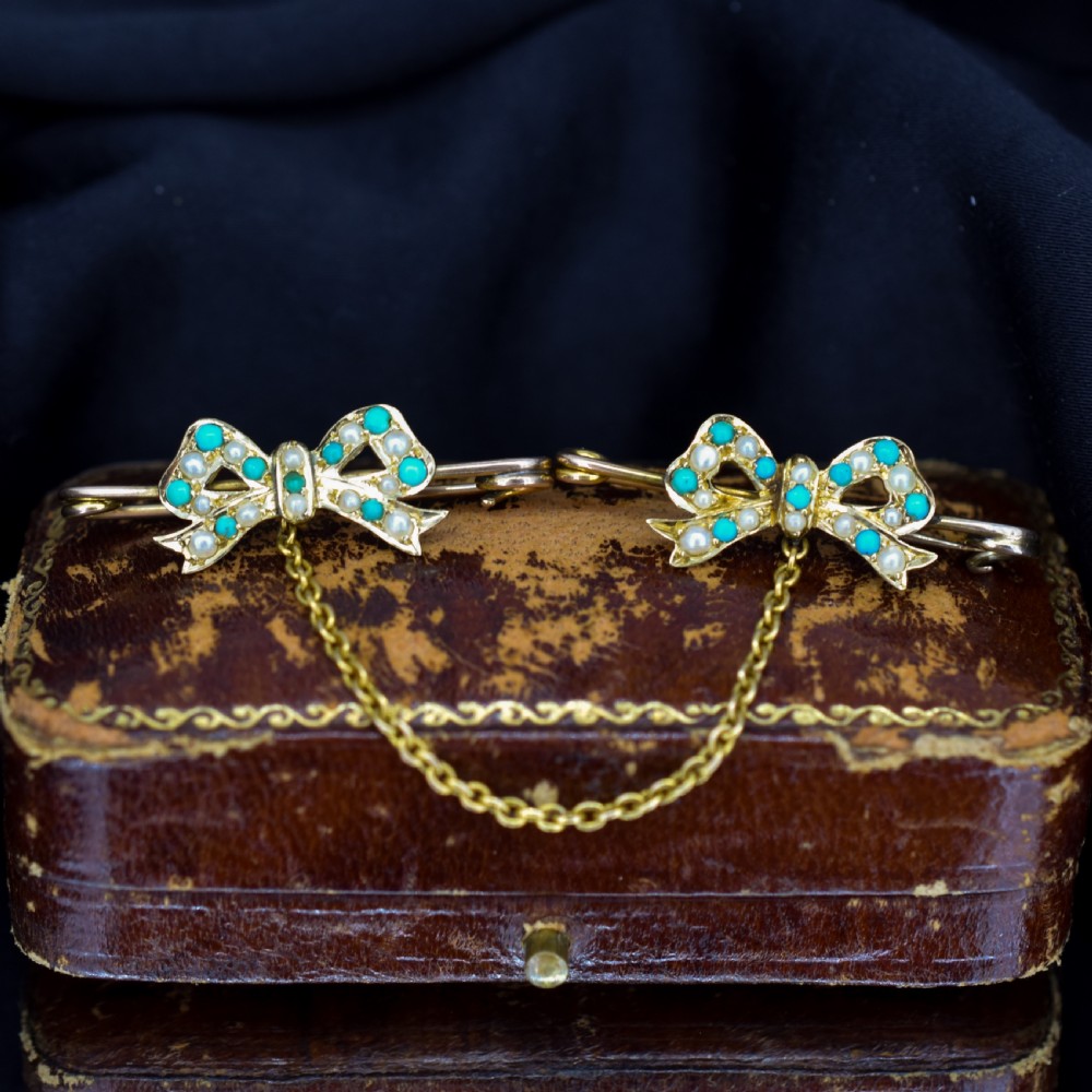 A pair of 15ct gold bow-shaped collar brooches set with seed pearls and turquoise cabochons, linked together by a delicate gold trace chain.