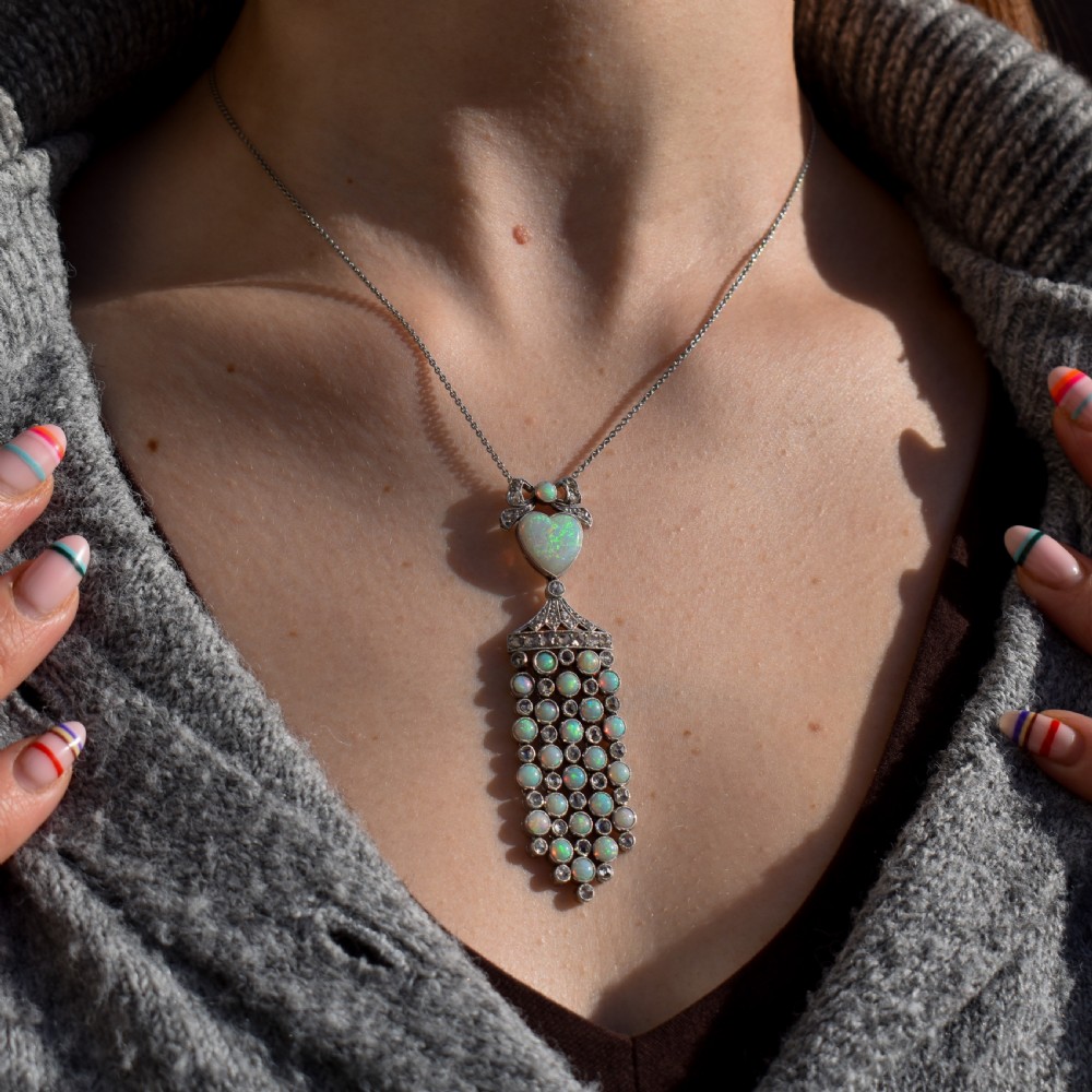 An Art Deco platinum and white gold pendant necklace featuring a bow motif, a heart-shaped opal cabochon, and a tassel drop set with opals and diamonds. View II