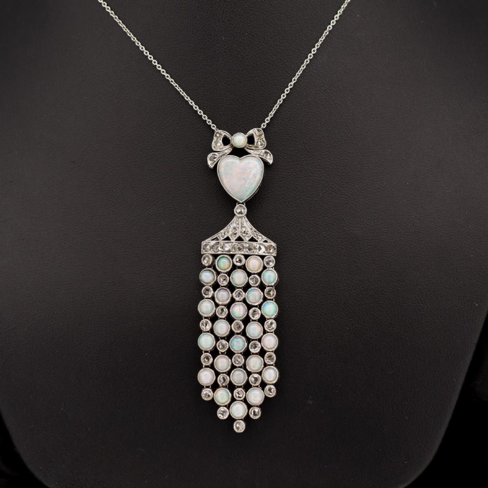 An Art Deco platinum and white gold pendant necklace featuring a bow motif, a heart-shaped opal cabochon, and a tassel drop set with opals and diamonds. View III