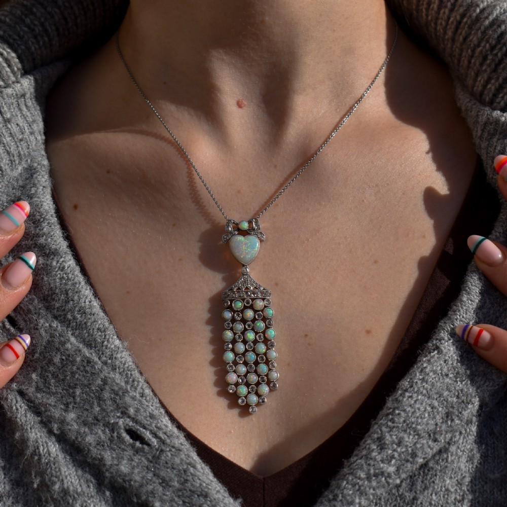 An Art Deco platinum and white gold pendant necklace featuring a bow motif, a heart-shaped opal cabochon, and a tassel drop set with opals and diamonds. View IV