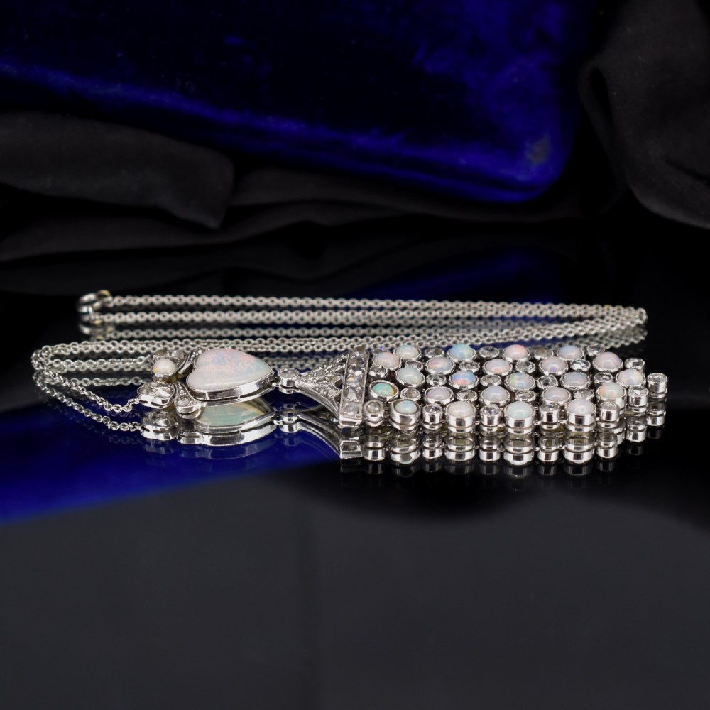 An Art Deco platinum and white gold pendant necklace featuring a bow motif, a heart-shaped opal cabochon, and a tassel drop set with opals and diamonds. View VII