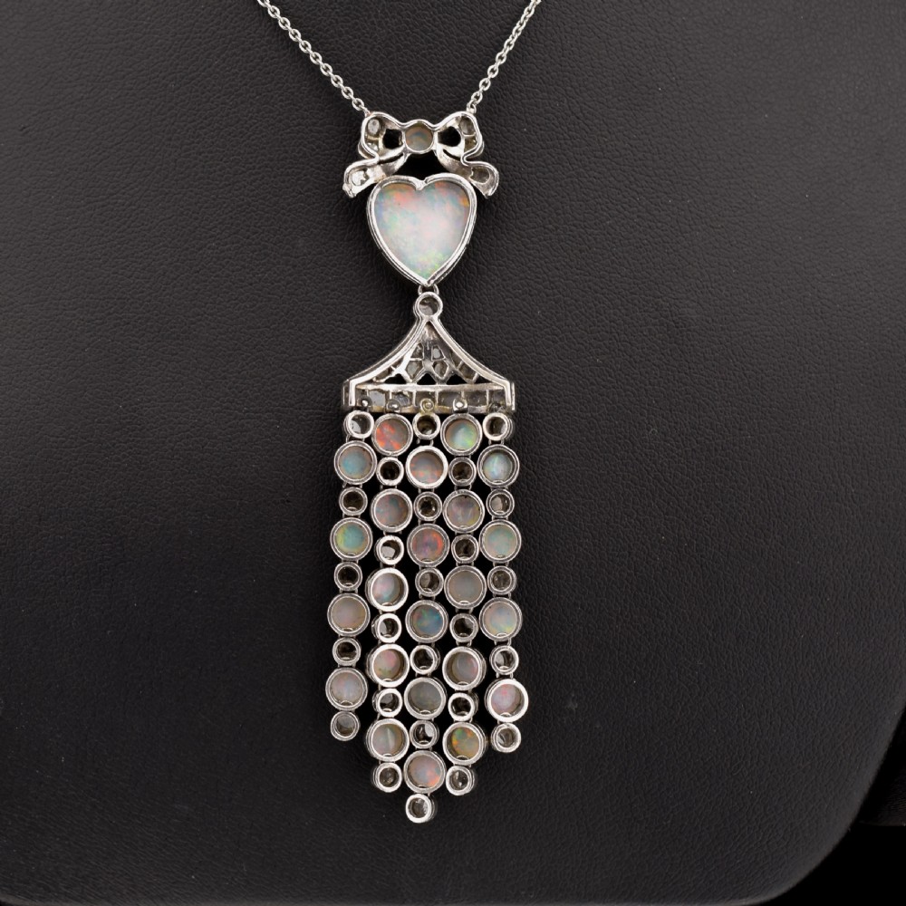 An Art Deco platinum and white gold pendant necklace featuring a bow motif, a heart-shaped opal cabochon, and a tassel drop set with opals and diamonds. View VIII