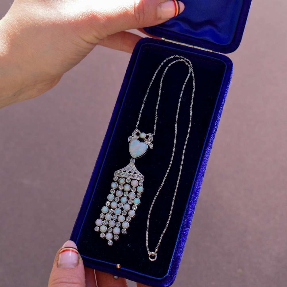An Art Deco platinum and white gold pendant necklace featuring a bow motif, a heart-shaped opal cabochon, and a tassel drop set with opals and diamonds. View XI