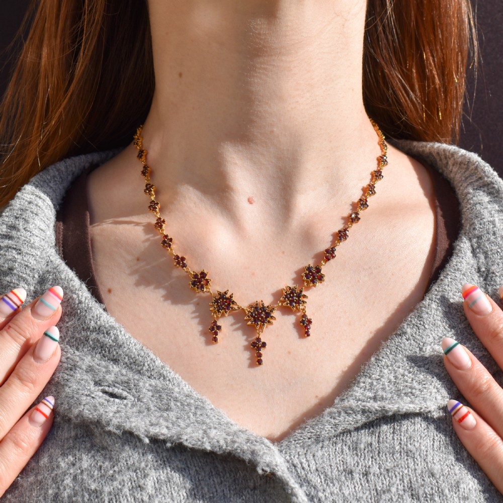 A Victorian gold gilt necklace set with deep red rose-cut Bohemian garnets featuring starburst clusters and drop pendants. View II