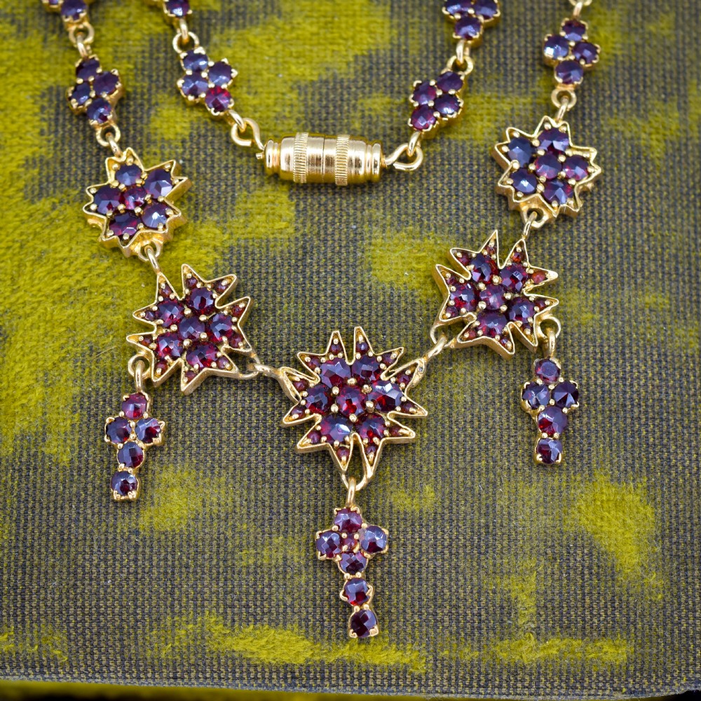 A Victorian gold gilt necklace set with deep red rose-cut Bohemian garnets featuring starburst clusters and drop pendants. View V