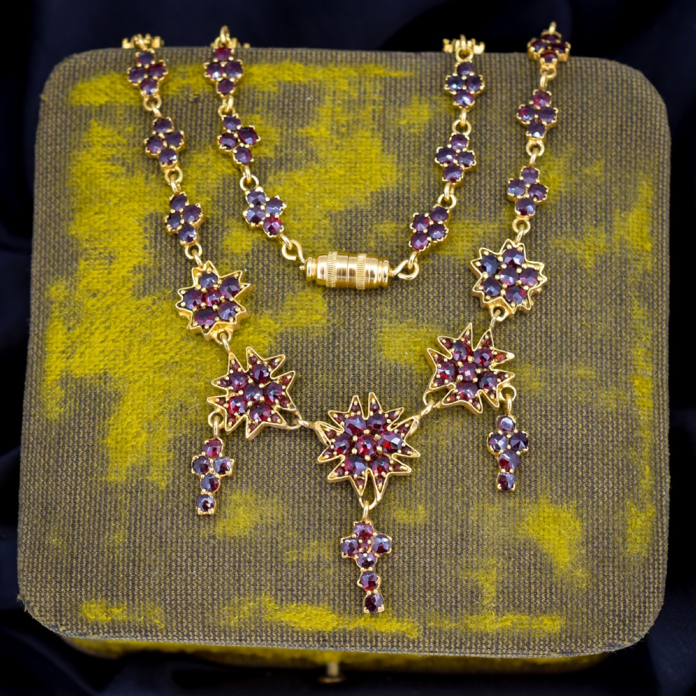 A Victorian gold gilt necklace set with deep red rose-cut Bohemian garnets featuring starburst clusters and drop pendants. View VI