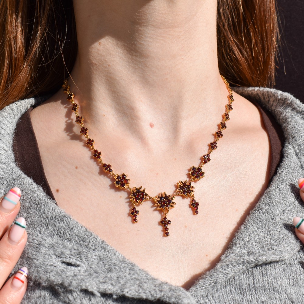 A Victorian gold gilt necklace set with deep red rose-cut Bohemian garnets featuring starburst clusters and drop pendants. View VII