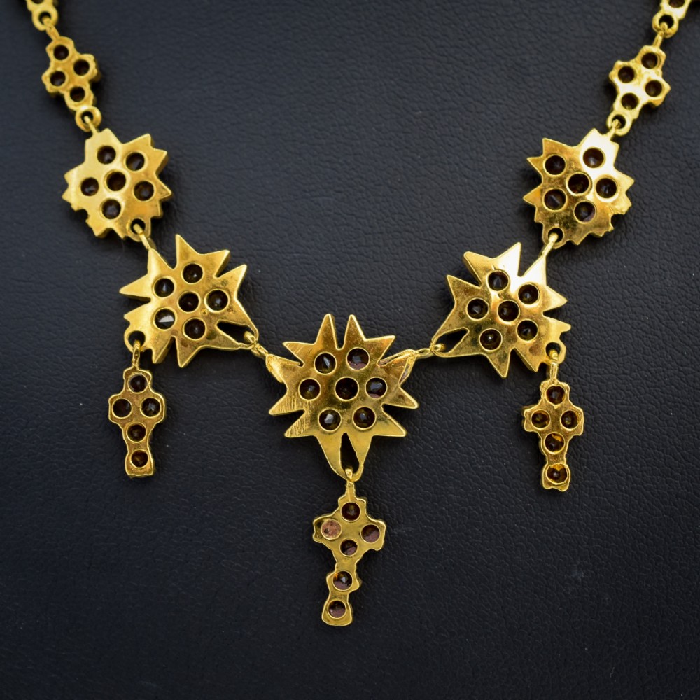 A Victorian gold gilt necklace set with deep red rose-cut Bohemian garnets featuring starburst clusters and drop pendants. View IX