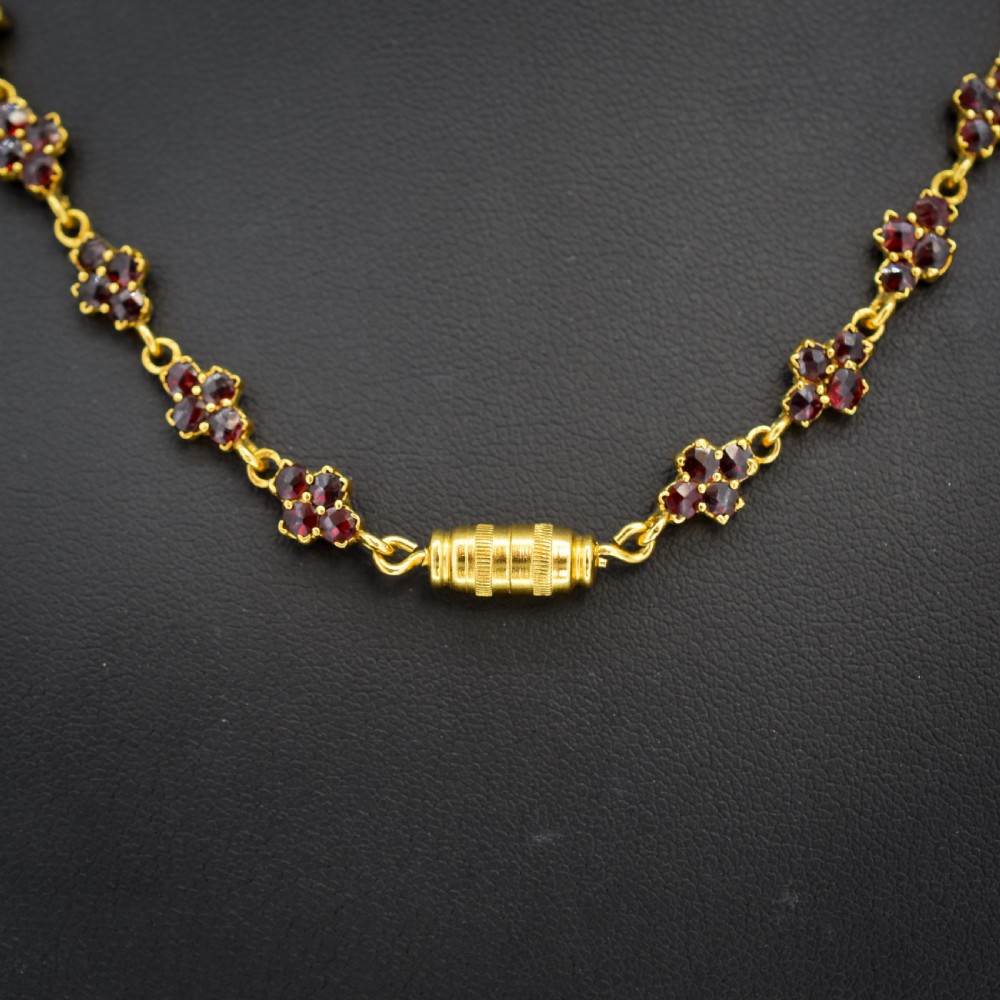 A Victorian gold gilt necklace set with deep red rose-cut Bohemian garnets featuring starburst clusters and drop pendants. View X