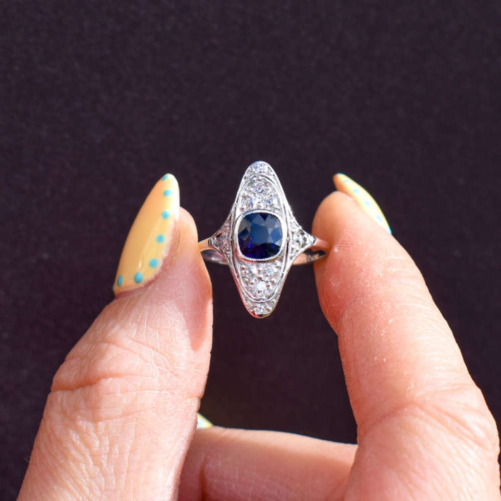 An Art Deco platinum ring featuring a central blue sapphire framed by diamonds within an elongated navette-shaped setting. View III