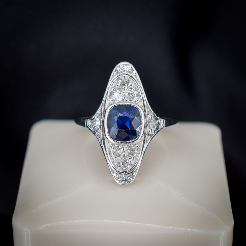 An Art Deco platinum ring featuring a central blue sapphire framed by diamonds within an elongated navette-shaped setting. View IV
