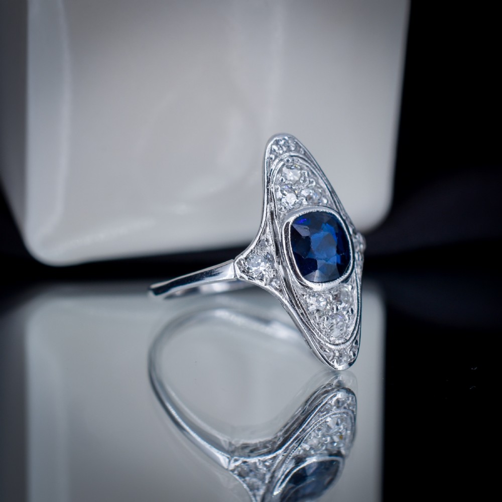An Art Deco platinum ring featuring a central blue sapphire framed by diamonds within an elongated navette-shaped setting. View VI