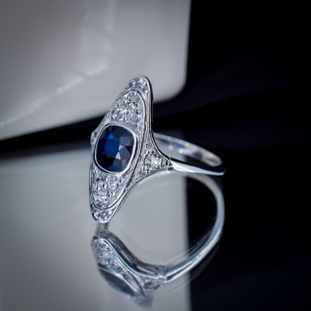 An Art Deco platinum ring featuring a central blue sapphire framed by diamonds within an elongated navette-shaped setting. View VII