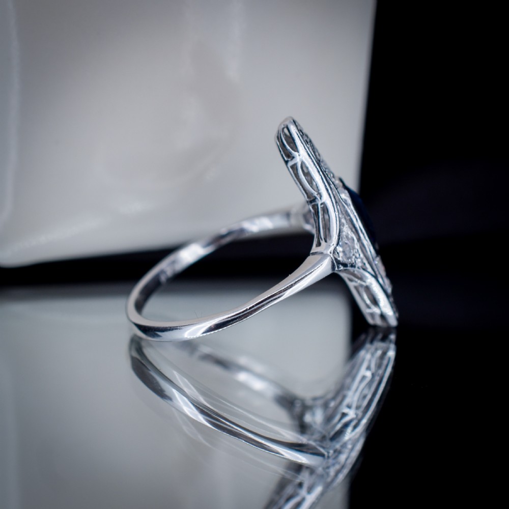 An Art Deco platinum ring featuring a central blue sapphire framed by diamonds within an elongated navette-shaped setting. View VIII