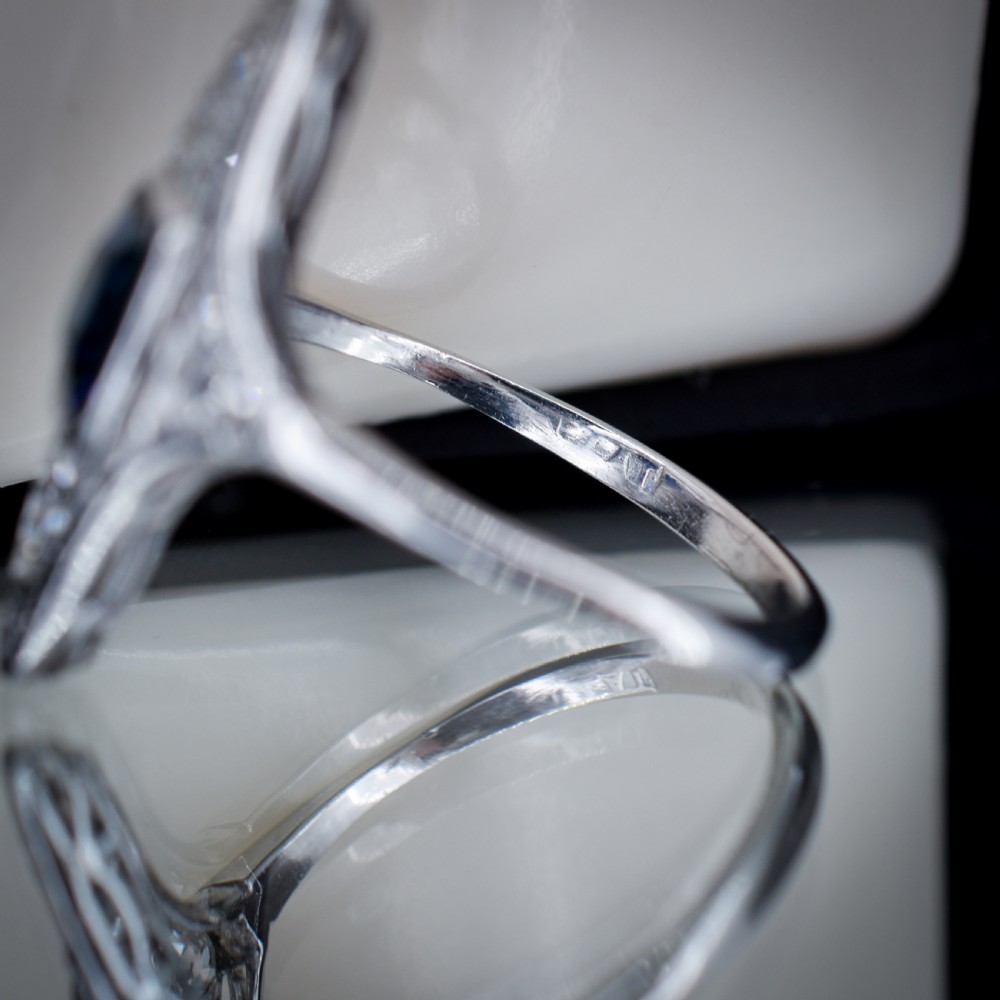 An Art Deco platinum ring featuring a central blue sapphire framed by diamonds within an elongated navette-shaped setting. View X