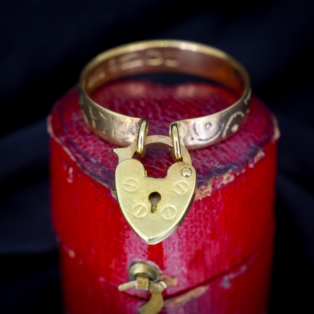 An engraved 9ct yellow gold band featuring a dangling heart padlock charm.