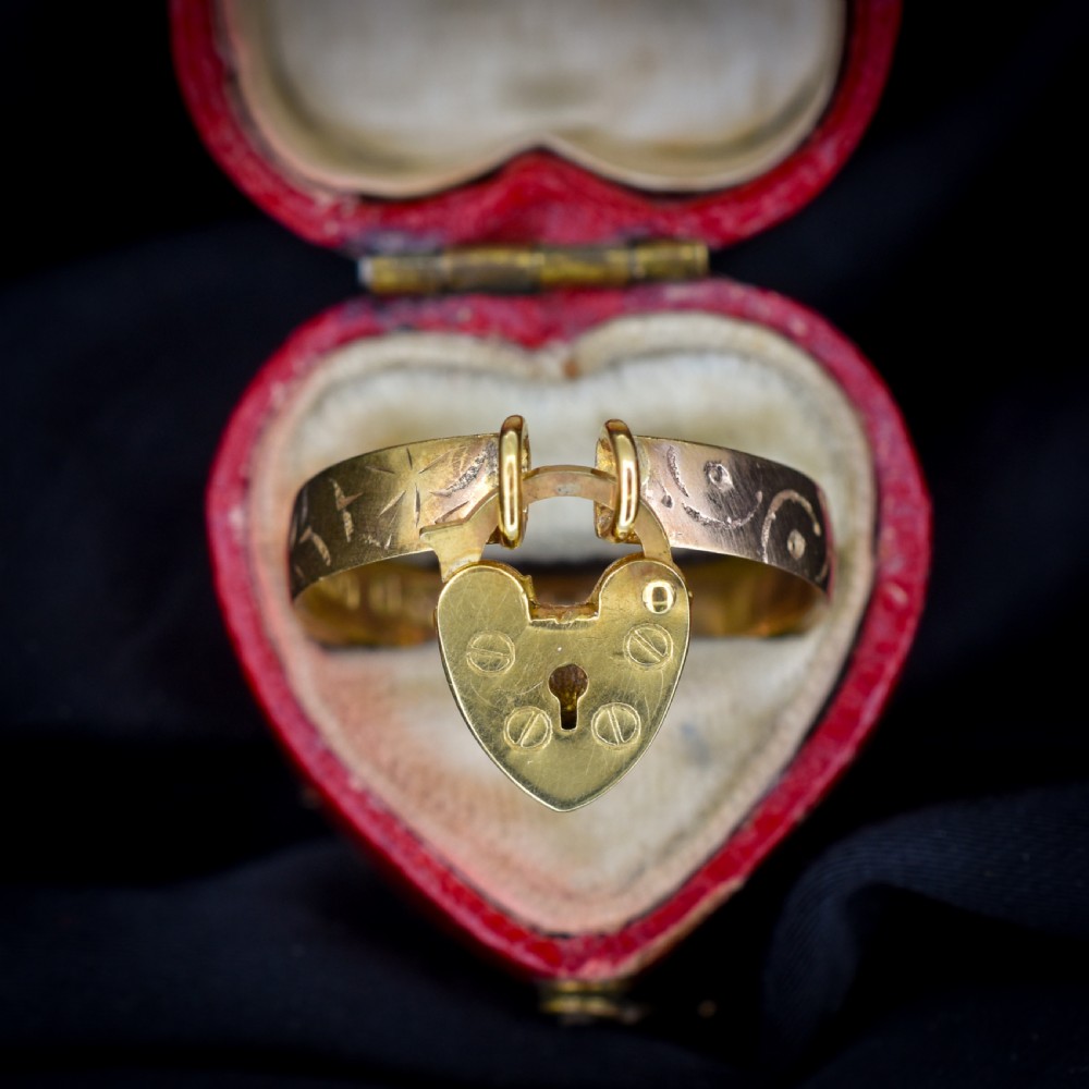 An engraved 9ct yellow gold band featuring a dangling heart padlock charm. View VI