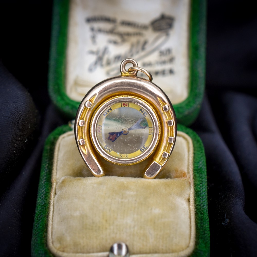 An antique yellow gold horseshoe pendant enclosing a central working compass with a glass face and suspension loop.