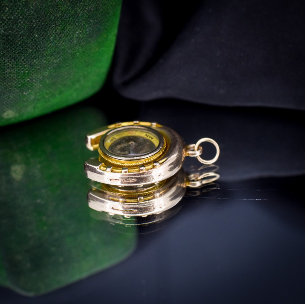 An antique yellow gold horseshoe pendant enclosing a central working compass with a glass face and suspension loop. View IX