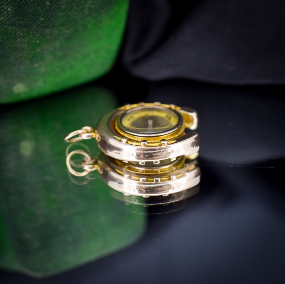 An antique yellow gold horseshoe pendant enclosing a central working compass with a glass face and suspension loop. View XI