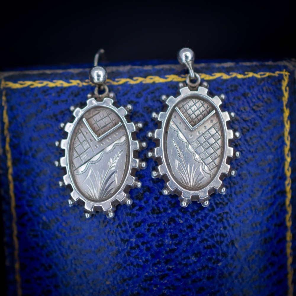 A pair of oval sterling silver Victorian Aesthetic Movement drop earrings featuring engraved geometric and botanical designs with beaded borders. View III