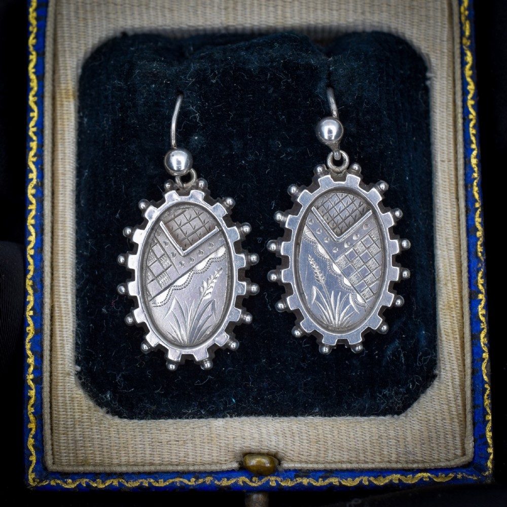 A pair of oval sterling silver Victorian Aesthetic Movement drop earrings featuring engraved geometric and botanical designs with beaded borders. View IV