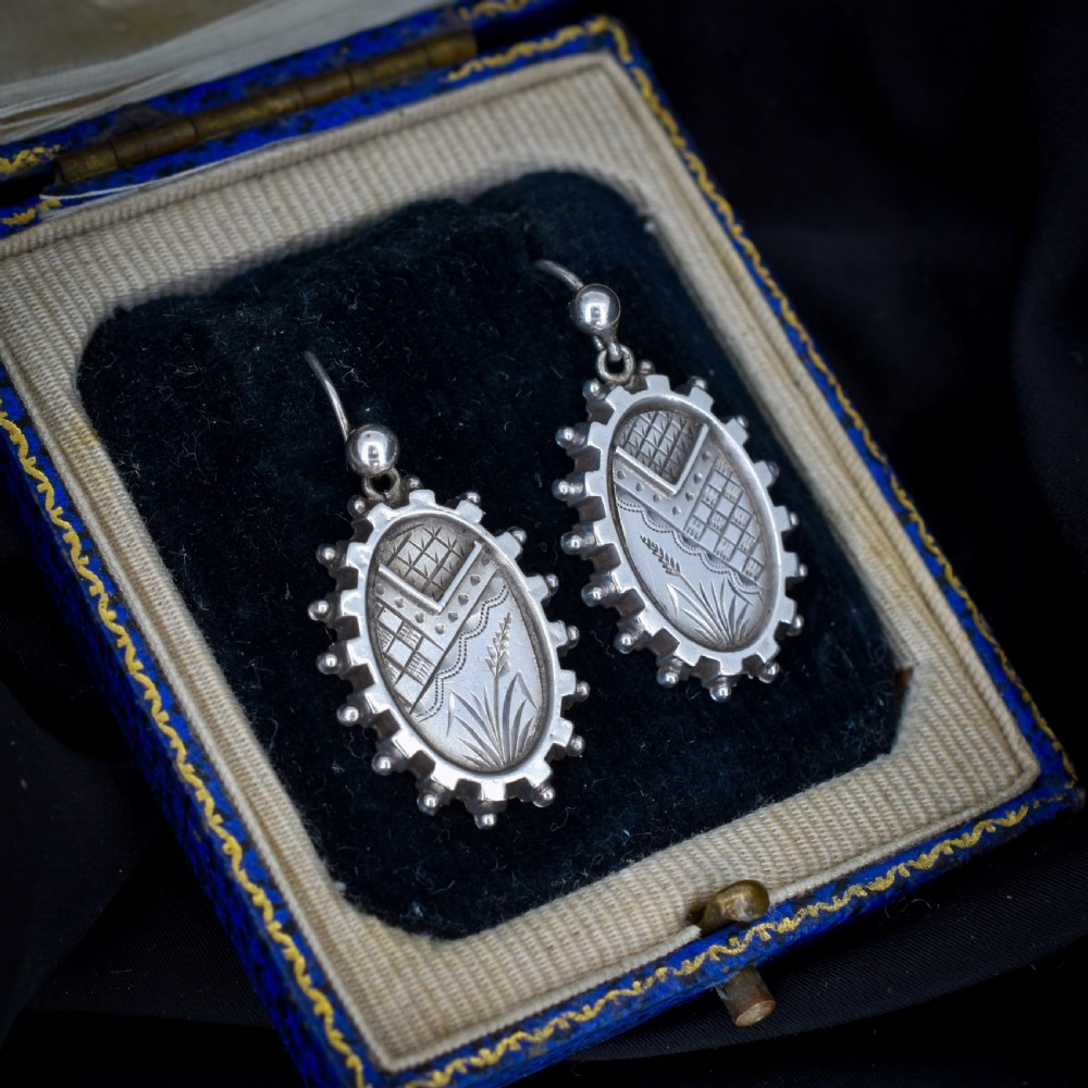 A pair of oval sterling silver Victorian Aesthetic Movement drop earrings featuring engraved geometric and botanical designs with beaded borders. View VI