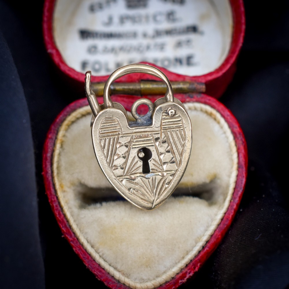 A vintage 9ct yellow gold heart-shaped padlock charm with geometric and botanical hand-engraved patterns and a keyhole detail.