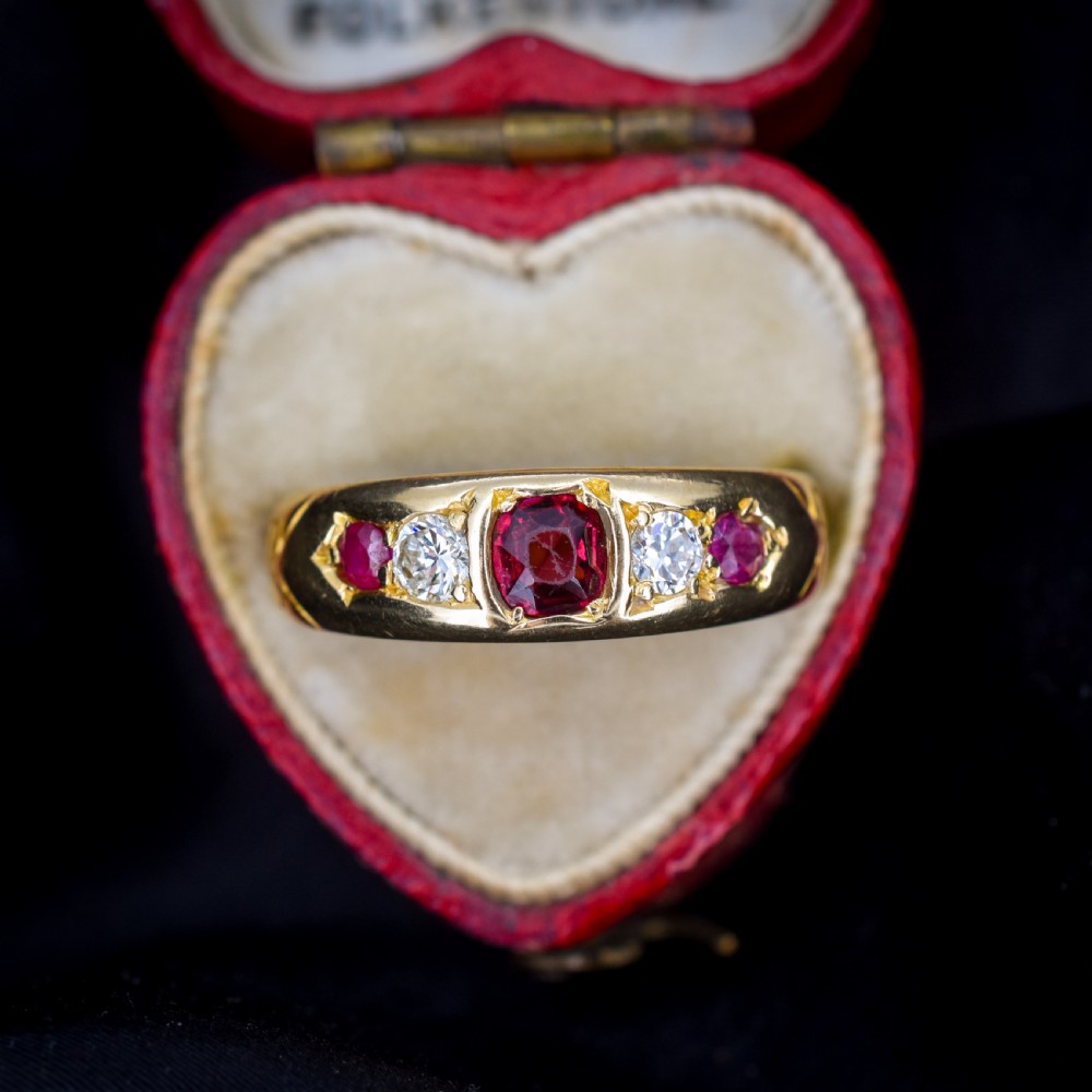 An 18ct yellow gold band ring set with five cushion and round faceted red rubies, garnets, and diamonds in flush settings.