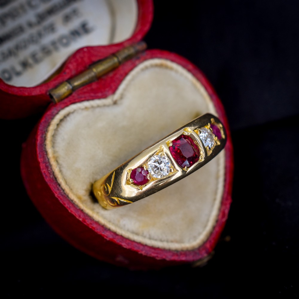 An 18ct yellow gold band ring set with five cushion and round faceted red rubies, garnets, and diamonds in flush settings. View III