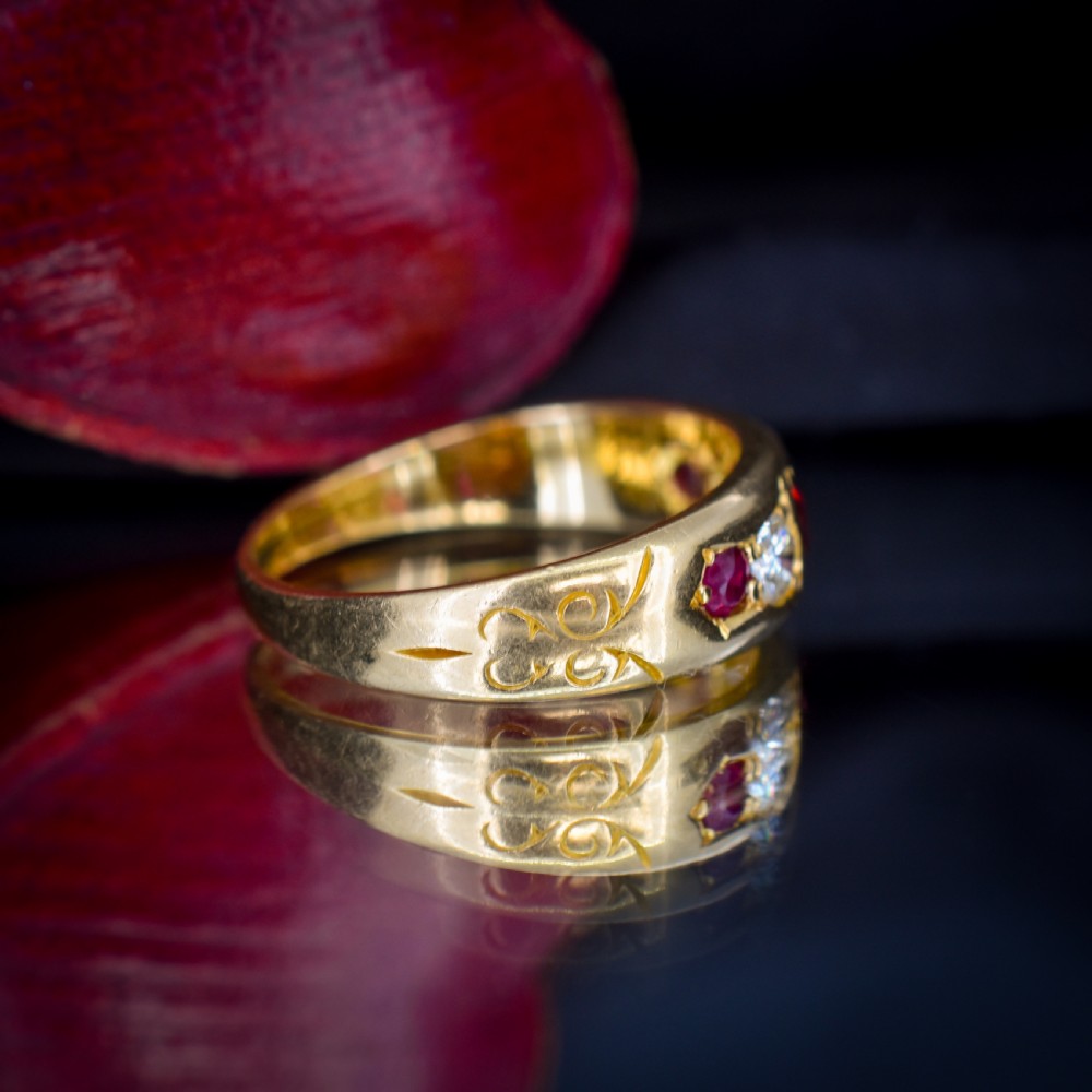 An 18ct yellow gold band ring set with five cushion and round faceted red rubies, garnets, and diamonds in flush settings. View V