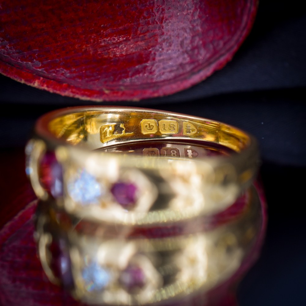 An 18ct yellow gold band ring set with five cushion and round faceted red rubies, garnets, and diamonds in flush settings. View VI