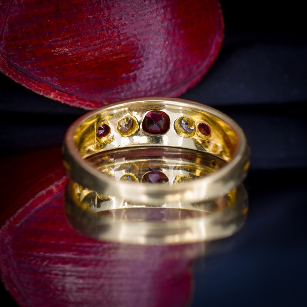 An 18ct yellow gold band ring set with five cushion and round faceted red rubies, garnets, and diamonds in flush settings. View VII